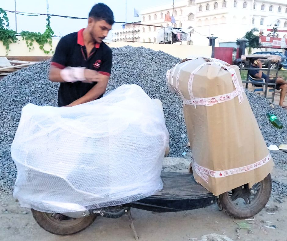 "Professional packers and movers worker wrapping a scooter with bubble wrap and cardboard for safe relocation – reliable Bike transport service ensuring safety and care."